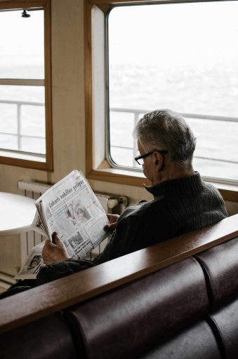 Senior reading newspaper while Sitting on a cruise.