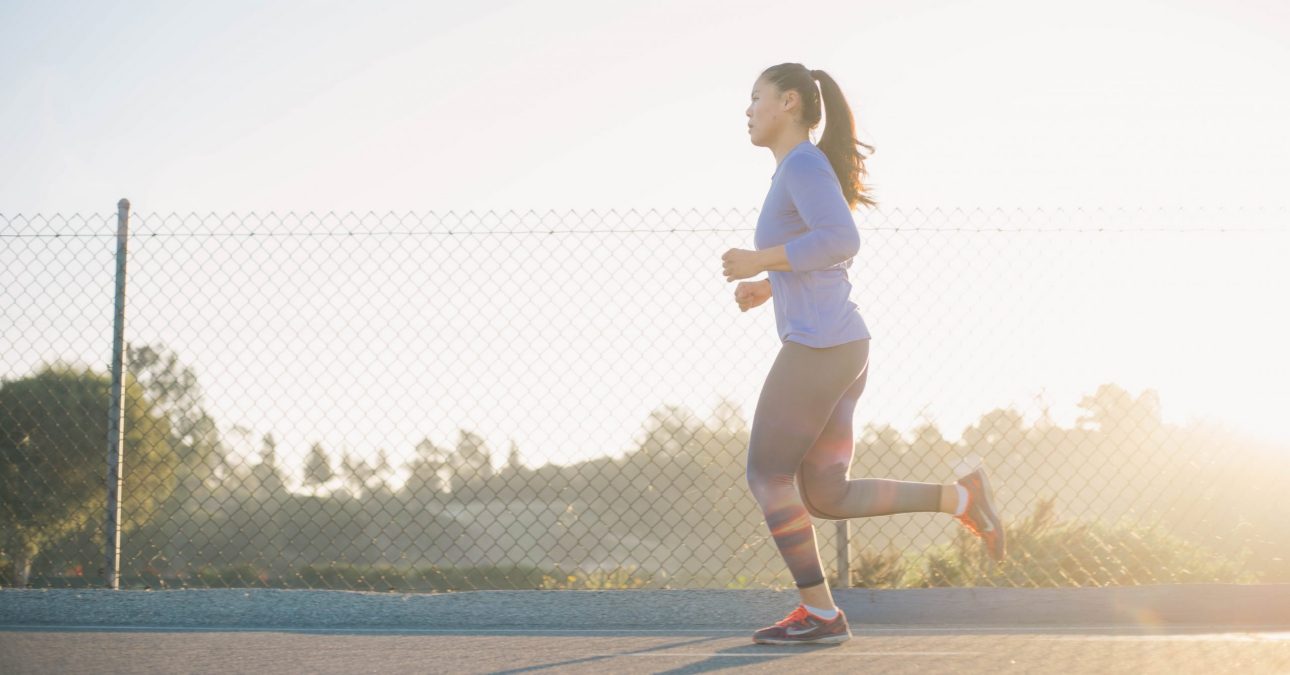 young woman jogging along the road side near wire fence