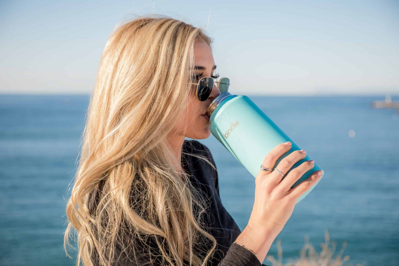 young woman drinking from a bottle by the sea