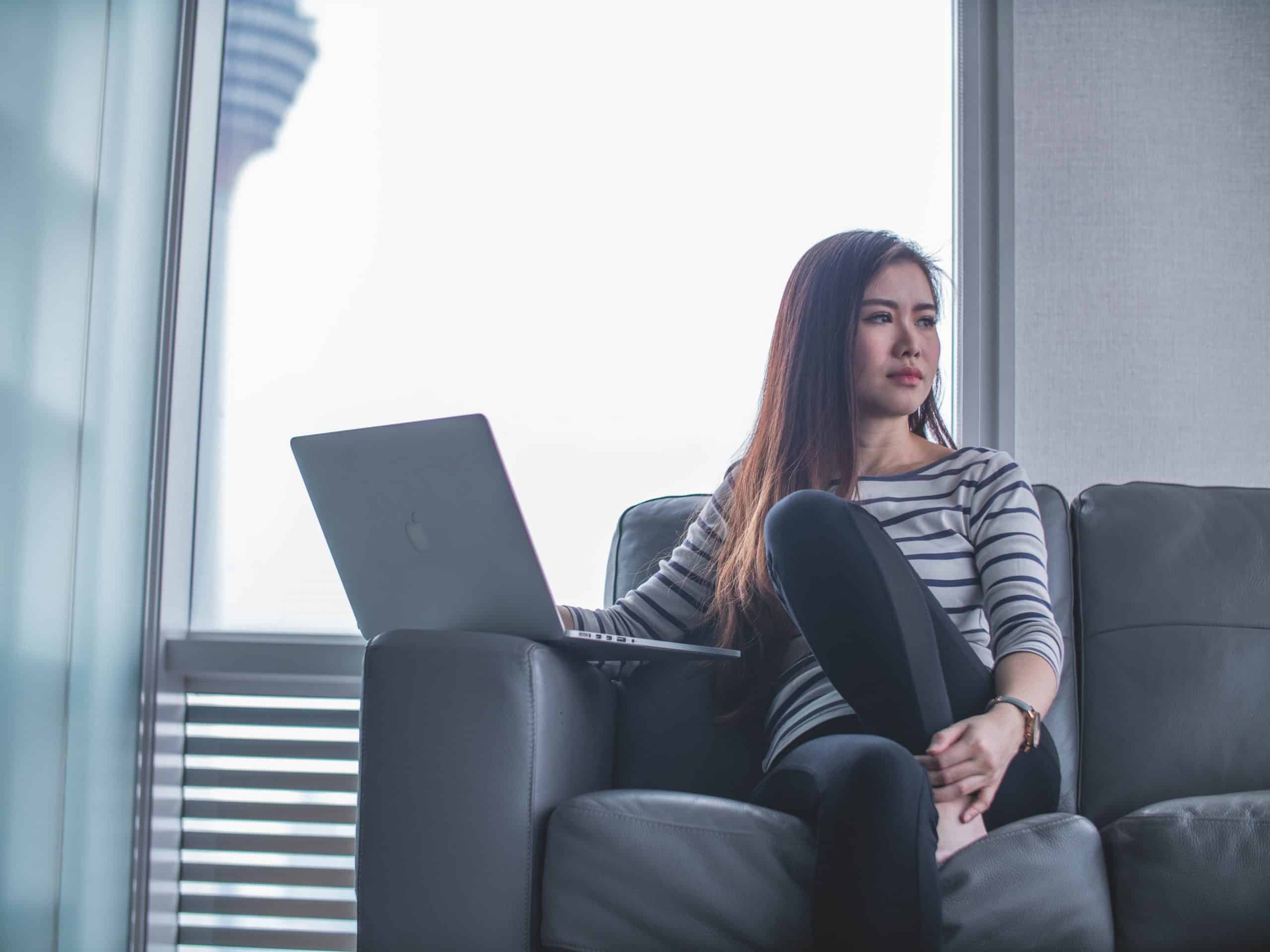 young asian woman lounging on a sofa with a laptop