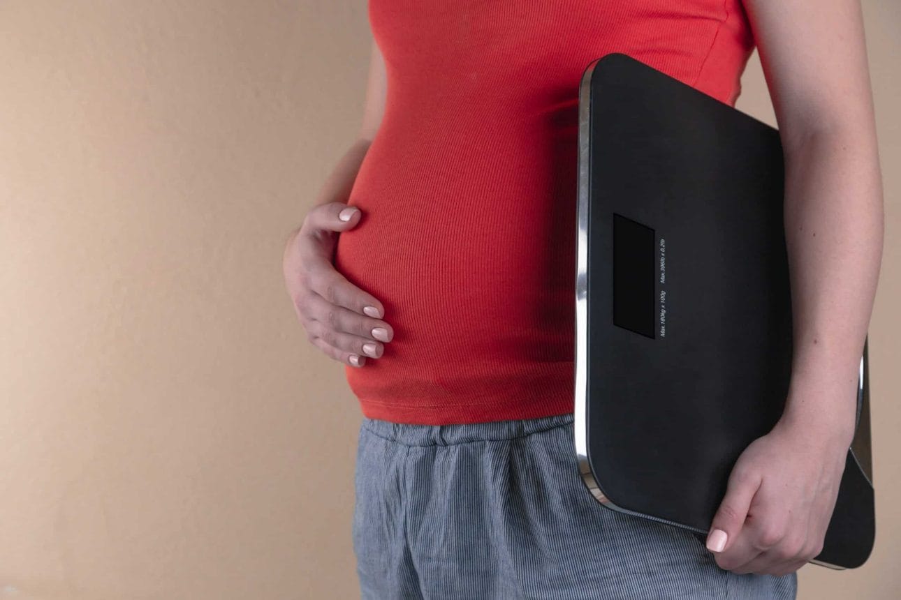 woman holding her belly and weighing scale